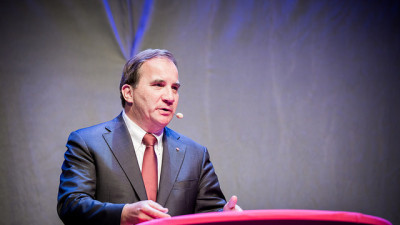 Stefan Löfven står i en talarstol. Han har kort hår, slips och en mikrofon vid munnen.