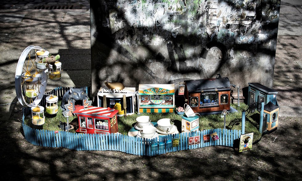 Ett tivoli i miniatyrformat. Tivolit har flera små bodar och ett pariserhjul. Det är omgärdat av ett blått staket och över ingången är en skylt där det står ”Tjoffsans tivoli”.