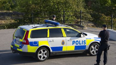 Två poliser står vid en polisbil.
