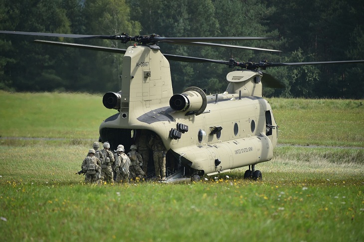 En grön stor helikopter står på en gräsmatta. Flera soldater håller på att gå in i helikoptern.