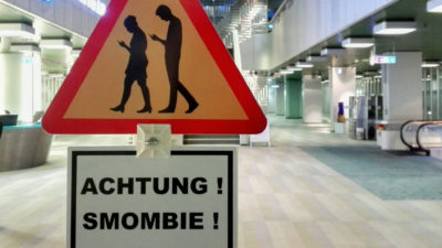 En varningsskylt med två människor som tittar ner i sina mobiltelefoner.