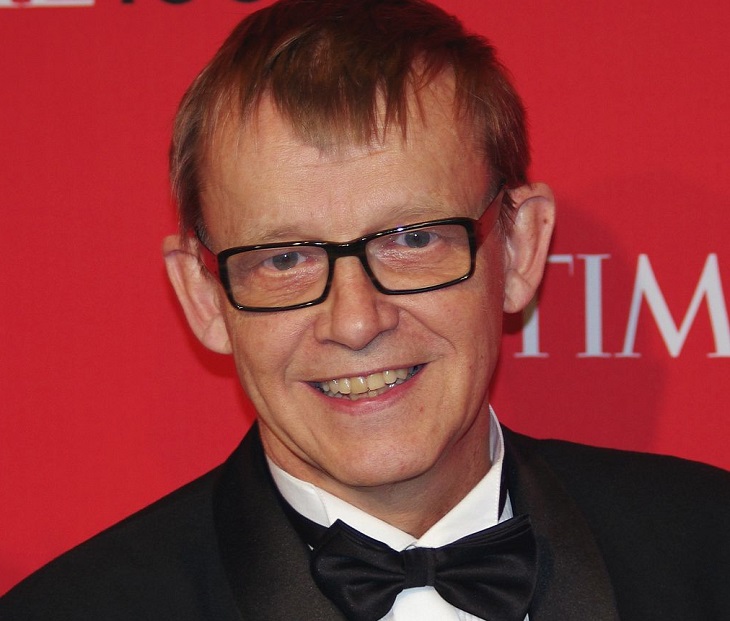 Hans Rosling tittar in i kameran. Han ser ut att vara i övre medelåldern. Han har kavaj och fluga på sig. Han har glasögon och ganska tunt kort hår som ligger kammat framåt. Hans tänder är gula och han har ganska stora öron.