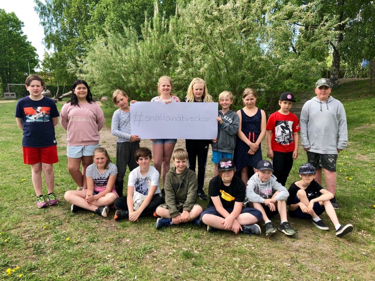 15 skolbarn på en gräsmatta håller i en skylt med texten #snällanätveckan.