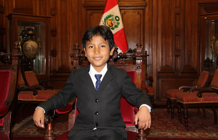 José sitter i en stor trästol. Han har kostym och slips på sig. Han har svart kort hår som är delat i en mittbena och ler mot kameran. I bakgrunden syns Perus flagga.