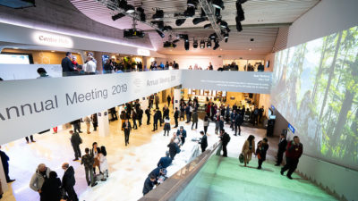 Många människor står utsprida i en stor foajé. Några står på en balkong över de andra. På balkongens sida står det "Annual meeting 2019".